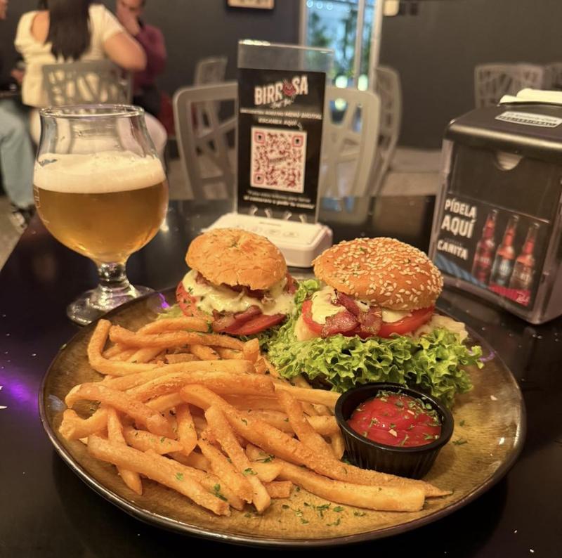 Mesa de Birrosa con dos hamburguesas, papas fritas, una copa de cerveza y el QR del menú digital